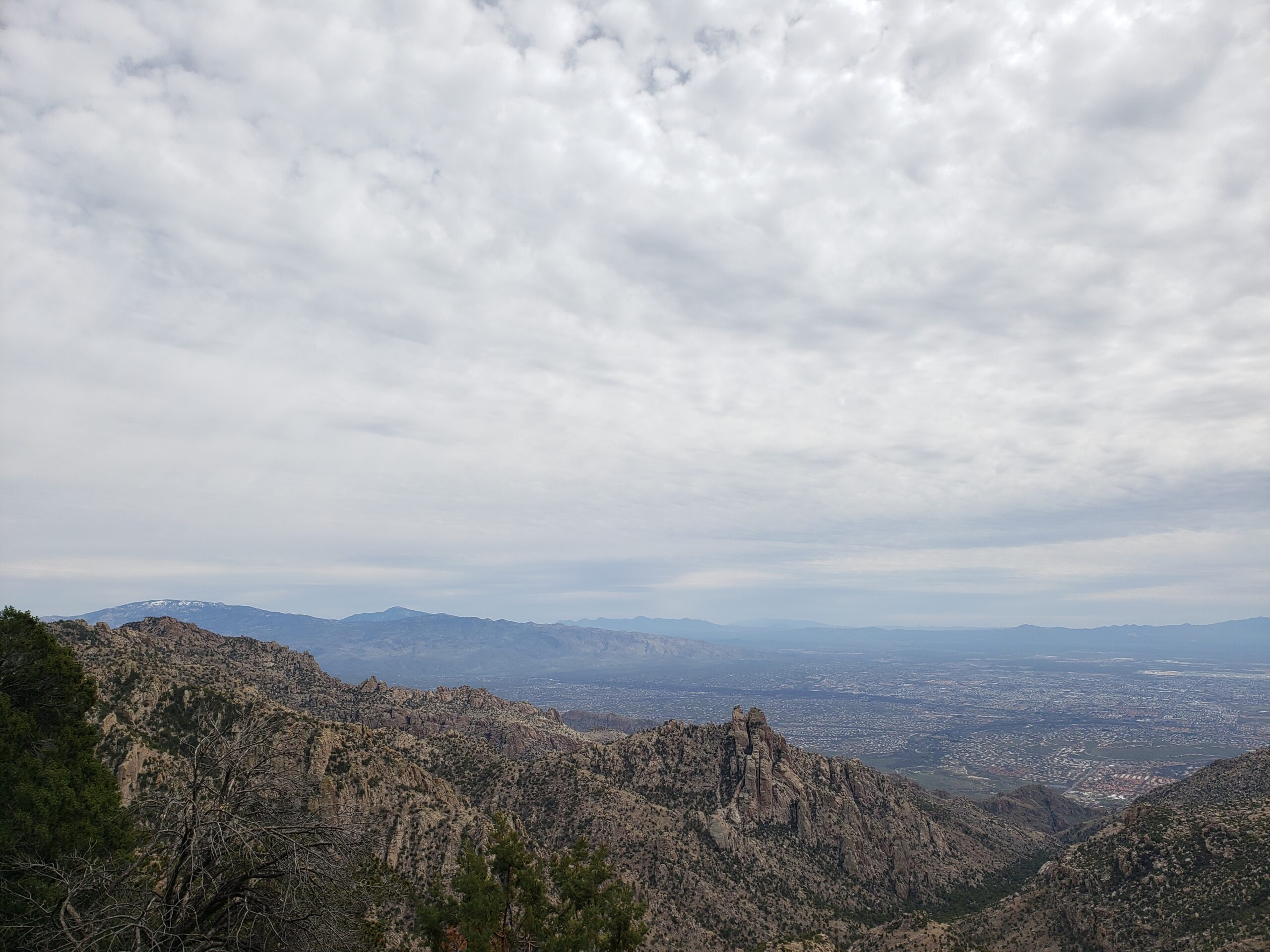 View from Cathedral Rock Trail in Tucson, Arizona. Clouds fill the sky over a view of the valley and front range of the Santa Catalina Mountains.